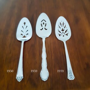 Può includere: Tre cucchiai da torta d'argento con diversi disegni e date segnate sulla superficie in legno: 1950, 1959 e 1939.