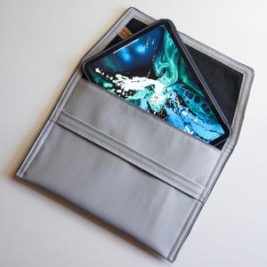 Peut inclure: Une pochette pour tablette en cuir gris avec un intérieur noir. Une tablette avec un économiseur d'écran abstrait coloré est à l'intérieur de la pochette.