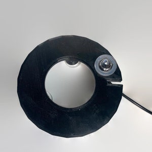 May include: Black plastic ring with a small silver screw in the top. The ring has a hole in the center.