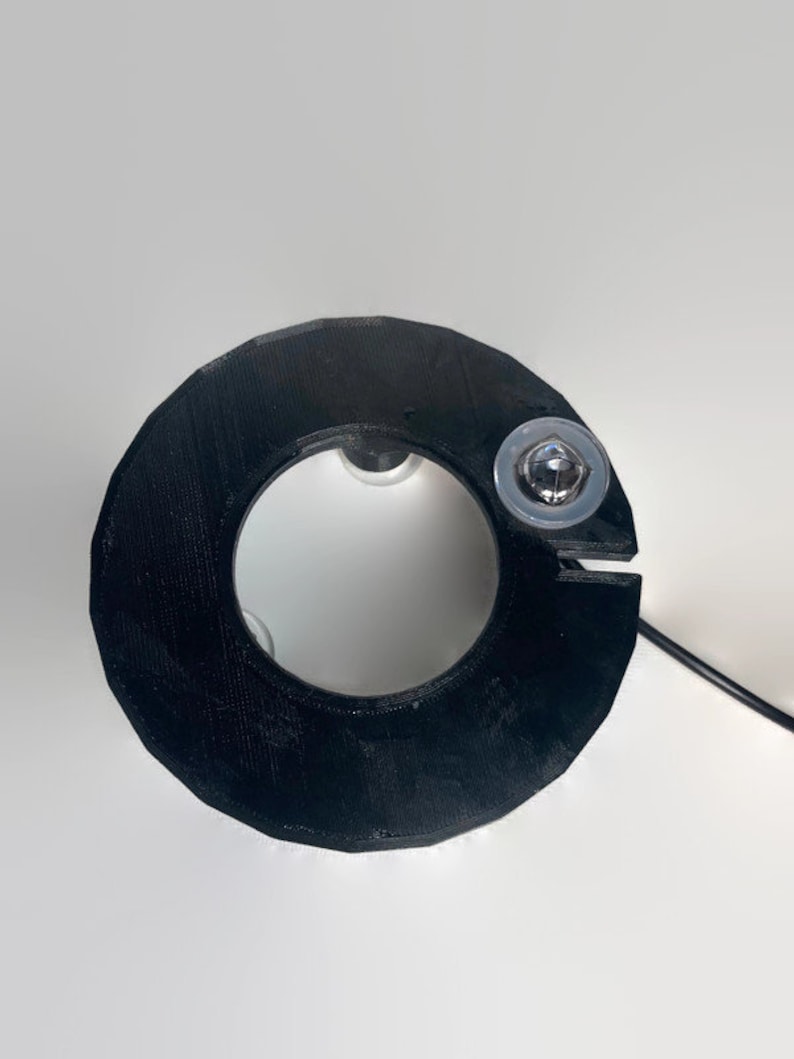 May include: Black plastic ring with a small silver screw in the top. The ring has a hole in the center.