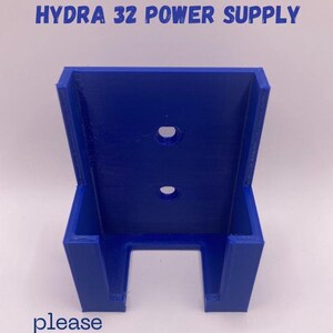 Puede incluir: Soporte de fuente de alimentaci&oacute;n azul vibrante impreso en 3D. El texto "HYDRA 32 POWER SUPPLY" est&aacute; impreso en la parte superior. El soporte tiene dos agujeros circulares y una abertura rectangular en la parte inferior. El texto "please rate us" est&aacute; impreso en la parte inferior.