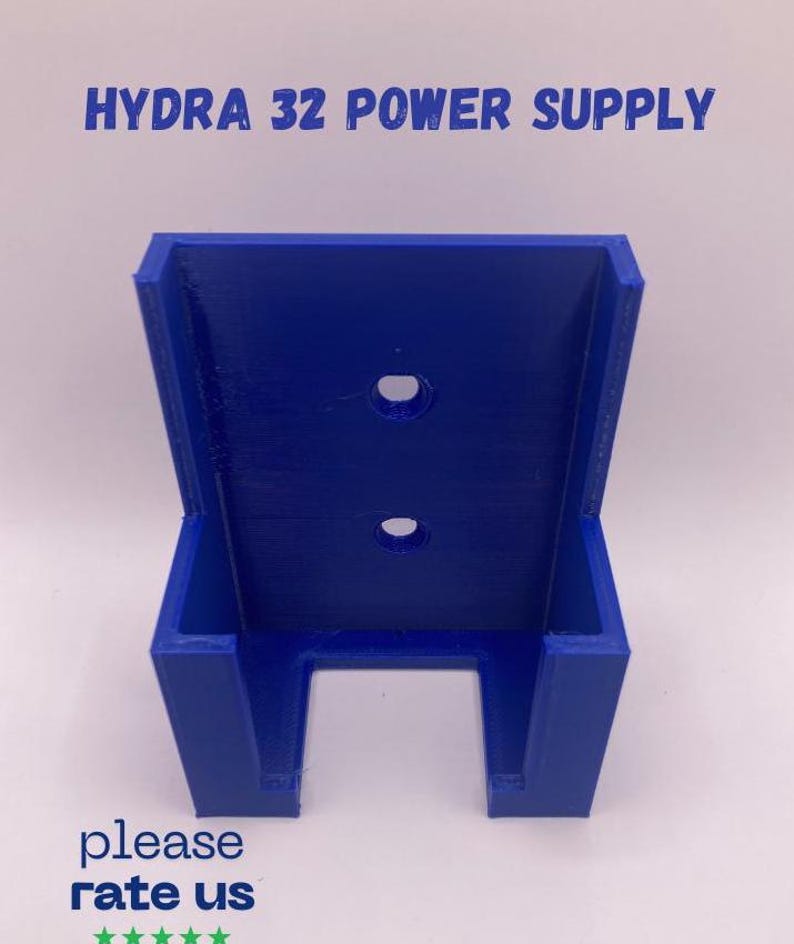 Puede incluir: Soporte de fuente de alimentaci&oacute;n azul vibrante impreso en 3D. El texto "HYDRA 32 POWER SUPPLY" est&aacute; impreso en la parte superior. El soporte tiene dos agujeros circulares y una abertura rectangular en la parte inferior. El texto "please rate us" est&aacute; impreso en la parte inferior.
