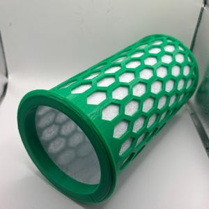 May include: A green, cylindrical filter with a honeycomb pattern and a white interior. The filter has a wide, circular rim at one end. The object is likely a replacement part for a machine or device.