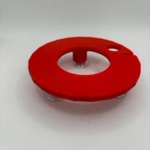 May include: A red plastic ring with suction cups on the bottom. The ring has a small hole in the top and a raised center.