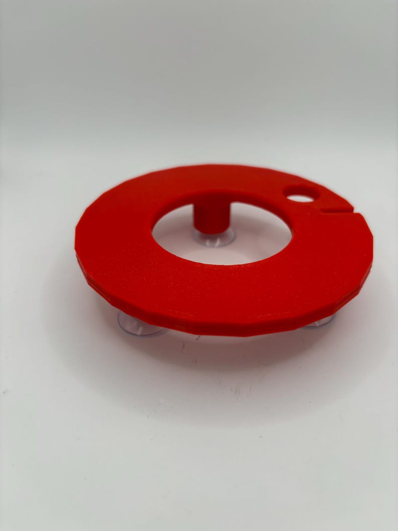 May include: A red plastic ring with suction cups on the bottom. The ring has a small hole in the top and a raised center.