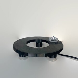 May include: A black circular base with suction cups on the bottom and a clear plastic top with a small, clear crystal on top. The base has a hole in the center.