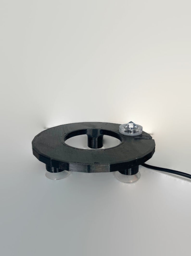 May include: A black circular base with suction cups on the bottom and a clear plastic top with a small, clear crystal on top. The base has a hole in the center.