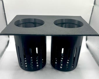 Può includere: Un portavasi in plastica nera con due aperture rotonde e due vasi in plastica nera con fori di drenaggio.