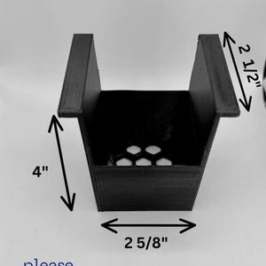 May include: Black plastic 3D printed object with a square base and a rectangular opening. The object measures 2 5/8 inches wide, 4 inches tall, and 2 1/2 inches deep.