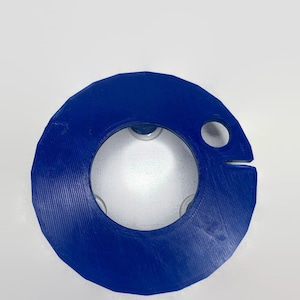 May include: A blue plastic ring with a hole in the center and a small hole on the side. The ring has a textured surface.
