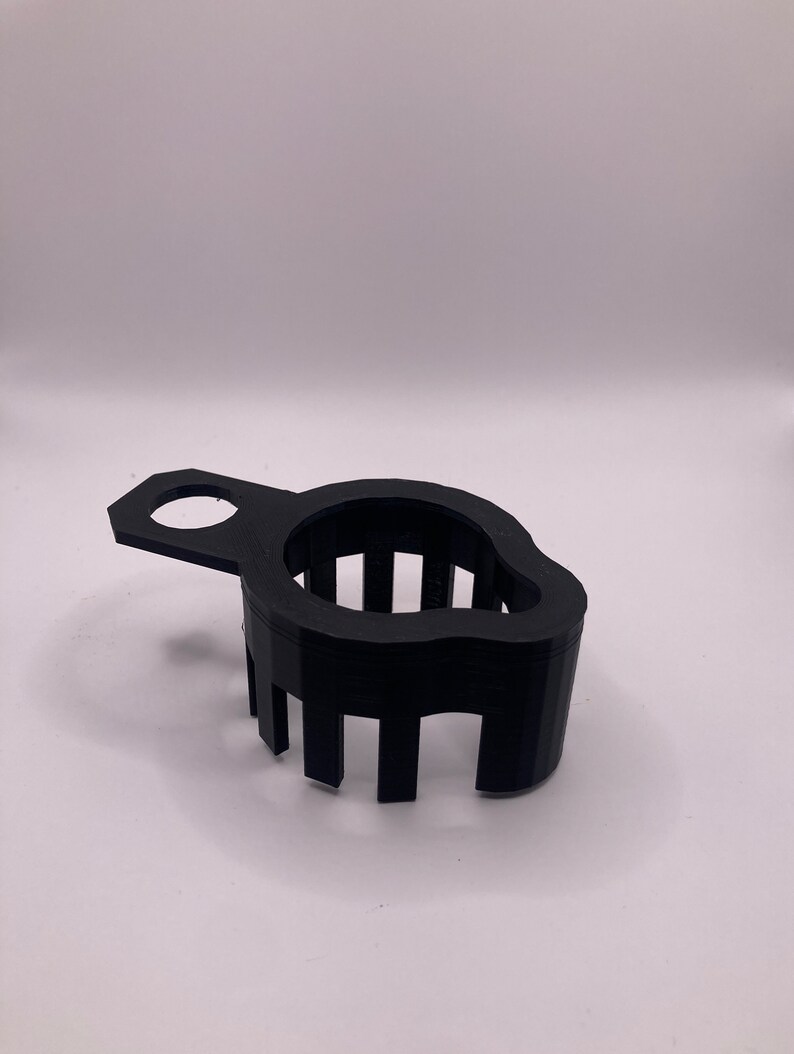 May include: A black plastic 3D printed tool with a handle and a series of vertical slots. The tool is designed to hold a round object.