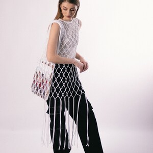 May include: A white crochet top with a long fringe and a black pair of pants. The top is a mesh design and the pants have cargo pockets.