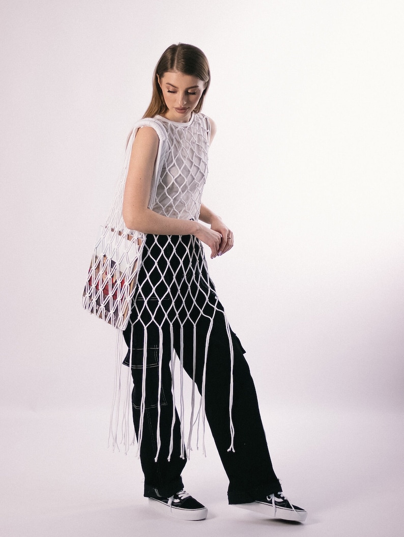 May include: A white crochet top with a long fringe and a black pair of pants. The top is a mesh design and the pants have cargo pockets.