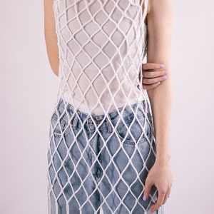 May include: A white crochet top with a loose, net-like design. The top is worn over a pair of light blue denim jeans.