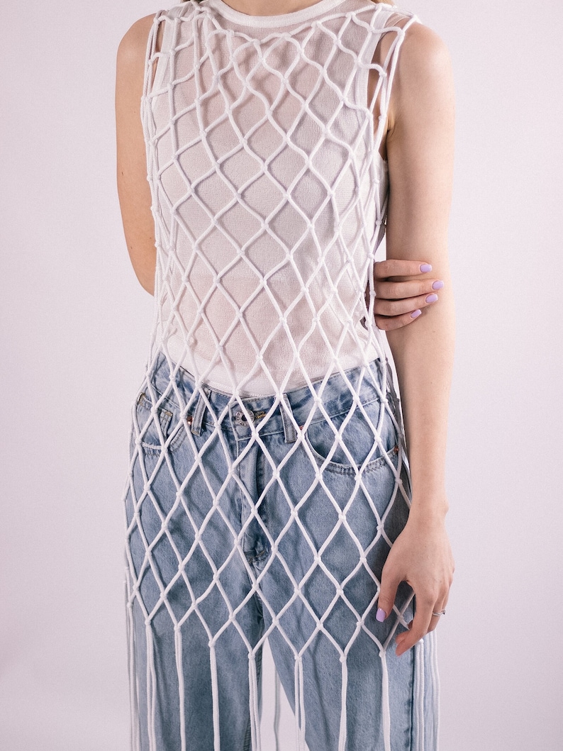 May include: A white crochet top with a loose, net-like design. The top is worn over a pair of light blue denim jeans.