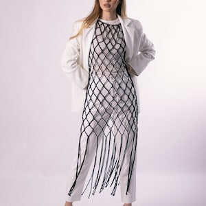 May include: A white blazer with a long, black, fringed mesh top and white pants. The model is wearing black heels.