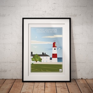 May include: Framed art print of Souter Lighthouse, Sunderland, Tyne and Wear. The image shows a red and white lighthouse, a white building, and a green lawn against a blue sky and sea. The print is in a black frame, displayed on a wooden floor.