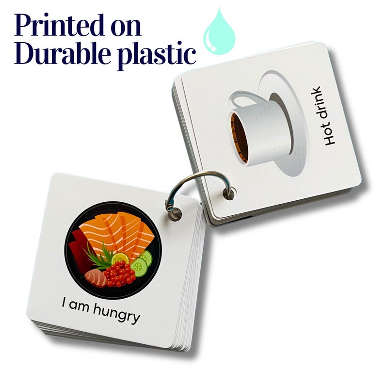 May include: A set of small, white, plastic flash cards with colorful illustrations and text. The cards are attached together with a silver ring. One card shows a bowl of sushi with the text "I am hungry". Another card shows a cup of coffee with the text "Hot drink".