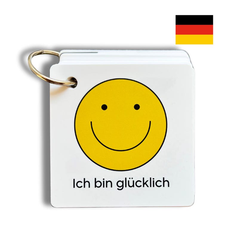 May include: A white card with a yellow smiley face and the text "Ich bin glücklich" in black. The card is attached to a silver ring.