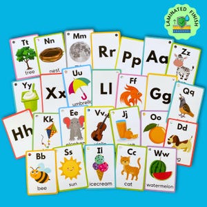May include: A set of colorful alphabet flash cards with illustrations and words. The cards feature letters from A to Z, with corresponding images and words like "tree", "nest", "umbrella", "violin", "cat", and "watermelon".