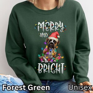 May include: Forest green unisex sweatshirt with a boxer dog wearing a Santa hat and surrounded by Christmas lights. The text "Merry and Bright" is printed on the sweatshirt.