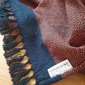 Peut inclure: Une écharpe tissée rouge et noire avec des franges noires et une étiquette qui indique "CocoLaine Atelier".