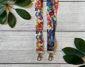 May include: Two colorful lanyards with cartoon character designs. The lanyard on the left features Winnie the Pooh characters, while the lanyard on the right features characters from Peter Pan. Both lanyards have silver swivel clips.