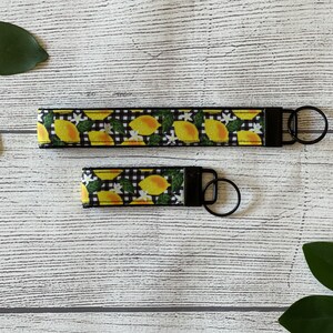 May include: A black and white lemon print key chain with a black metal ring. The key chain is made of fabric and has a black and white checkered pattern.