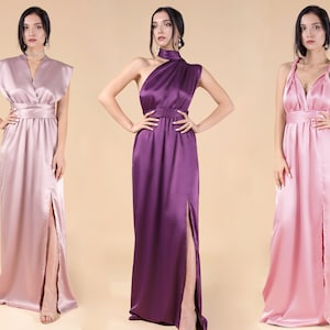 May include: Three women wearing long, flowing satin dresses in different colours: pink, purple, and light pink. The dresses have a V-neckline and a slit up the side. The women are standing in front of a beige background.