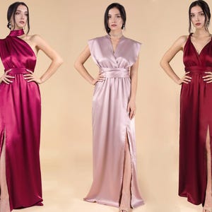 May include: Three women wearing long, flowing satin dresses in different colours: burgundy, blush pink, and maroon. The dresses have a wrap-style bodice and a thigh-high slit on one side.