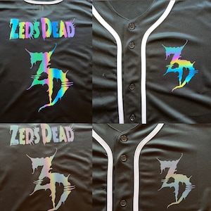 May include: Black baseball jersey with white piping and a rainbow iridescent logo that says "Zeds Dead" and a stylized "ZD" logo.