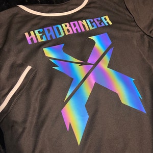 May include: Black baseball jersey with a white trim around the collar and sleeves. The back of the jersey features a large iridescent "X" with the text "HEADBANGER" above it.