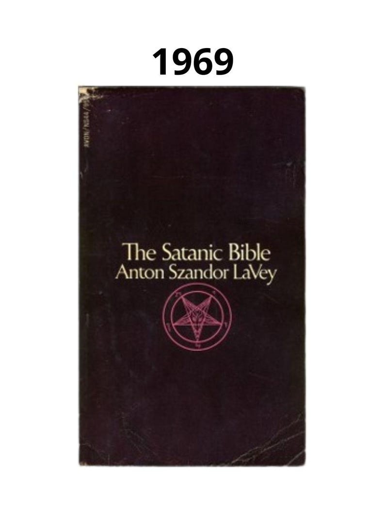 K&ouml;nnte beinhalten: Ein Vintage-Exemplar von "The Satanic Bible" von Anton Szandor LaVey. Das Buch hat einen dunkelburgunderfarbenen Einband mit dem Titel und dem Namen des Autors in Wei&szlig;. Ein rosa Pentagramm-Symbol ist mittig auf dem Einband platziert. Das Jahr "1969" ist oben aufgedruckt.