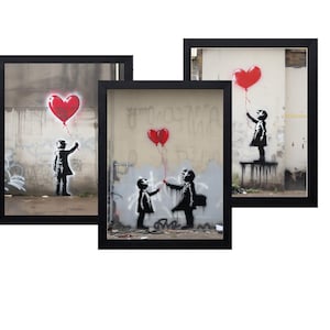 May include: Three framed Banksy prints featuring the iconic 'Girl with Balloon' artwork. Each print shows a black silhouette of a child reaching for a red heart-shaped balloon. The frames are black, and the backgrounds are urban scenes.