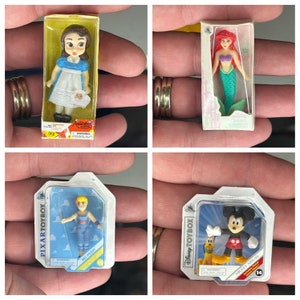 May include: Four small plastic figurines in clear plastic packaging. The figurines are of Disney characters: Alice, Ariel, Buzz Lightyear, and Mickey Mouse. The packaging includes the Disney Toybox logo and the Pixar Toybox logo.