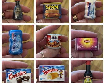 May include: A collection of miniature food items, including a can of SPAM, a box of Hostess CupCakes, a bottle of Kikkoman Soy Sauce, and a box of Lipton Ceylon Black Tea. Other items include Mentos gum and Dinty Moore Beef Stew.