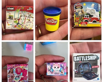 Może przedstawiać: Kolekcja miniaturowych zabawek, w tym park rozrywki K'nex, pojemnik Play-Doh, ciężarówka strażacka Play-Doh Wheels, zestaw do robienia biżuterii Sew Cool, pluszowa zabawka Hope the Alpaca i gra w okręty.