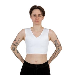 May include: White sleeveless undershirt with a V-neck. The undershirt is cropped and has a smooth, matte finish.