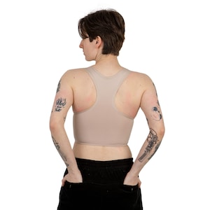 May include: A nude-colored racerback tank top with a scoop neck. The tank top is made of a soft, stretchy fabric and has a close fit.