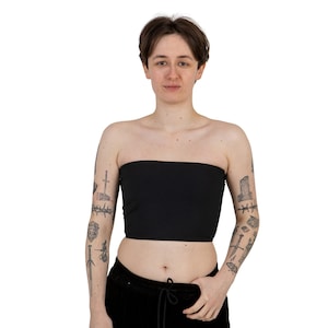 May include: A person wearing a black strapless top with a variety of tattoos on their arms.