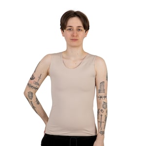 May include: A person wearing a light beige sleeveless tank top. The person has tattoos on both arms.