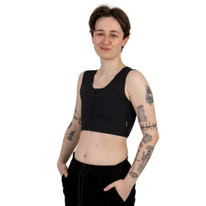 Puede incluir: Un top de compresión negro, sin mangas, con cremallera. El top es corto y tiene un acabado liso y mate.