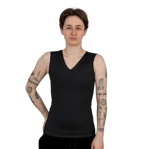 May include: A person wearing a black sleeveless v-neck shirt with a variety of tattoos on their arms.