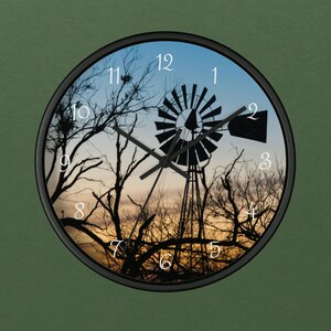 Könnte beinhalten: Eine schwarz-weiße Uhr mit einer Silhouette einer Windmühle und Bäumen vor einem Sonnenuntergang. Das Zifferblatt der Uhr hat römische Ziffern für die Stunden und schwarze Zeiger.