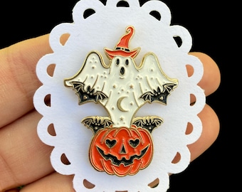 May include: A Halloween-themed enamel pin featuring a white ghost wearing a witch hat, with black bat wings, and a crescent moon. The ghost sits atop an orange jack-o'-lantern with heart-shaped eyes. The pin has gold-colored accents and is on a white, scalloped paper.