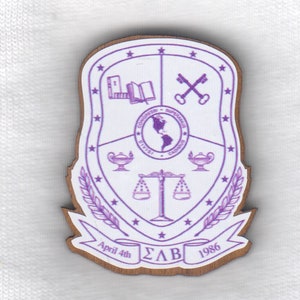 May include: A purple and white wooden crest with a shield design. The shield features a globe, a scale, a lamp, a book, and two keys. The crest also includes a banner with the text "April 4th ΣΛΒ 1986".