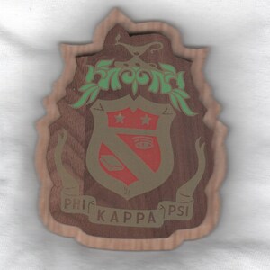 May include: Wooden plaque with a layered design featuring the Phi Kappa Psi fraternity crest. The crest is a shield shape with red, gold, and green accents, including stars, an eye, and a book. The words "PHI KAPPA PSI" are inscribed on the plaque.