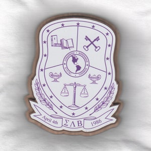 May include: A white shield with a purple border and purple symbols. The shield is divided into four sections. The top left section has a book, the top right section has two keys, the bottom left section has a lamp, and the bottom right section has a lamp. The shield is surrounded by a wreath of leaves and stars. The shield has the text "CONGRESSI • SUPERAMUS • DIVISI • CADIMUS" around the center. The shield also has the text "April 4th ΣΑΒ 1986" at the bottom.