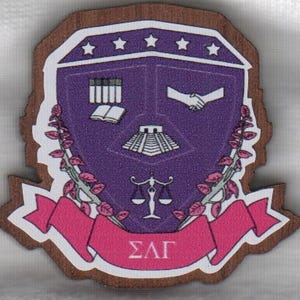 May include: A wooden emblem with a purple shield design, featuring a book, handshake, and scales of justice. A pink banner with Greek letters is at the bottom. The emblem is bordered by a brown wood grain.
