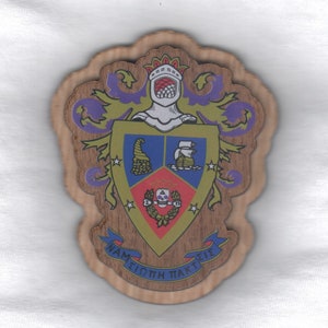 May include: A wooden plaque with a coat of arms design. The shield is divided into four sections, with a red, blue, and gold color scheme. The shield is surrounded by a gold crown and a purple and gold floral design. The text "NAM SIOTH PAKTI EIE" is written on a blue ribbon at the bottom of the plaque.